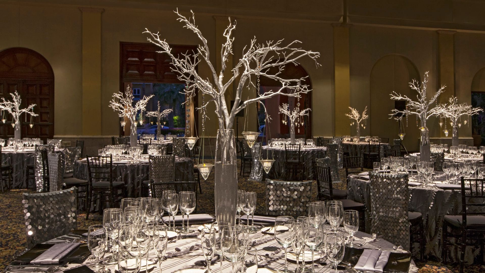 Elegantly set dining tables with silver decor and glass centerpieces in the Arcos 3 event room at Hacienda Del Mar Los Cabos in Cabo San Lucas.