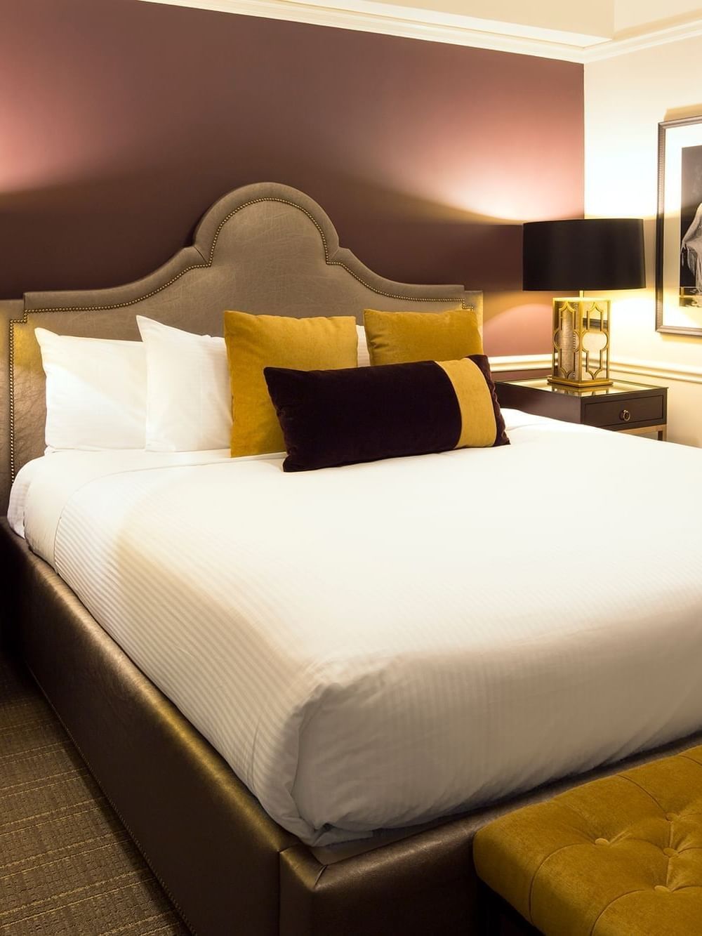 Bed between table lamps with gold pillows, and a deep purple accent wall behind in Follie Suite at Warwick New York