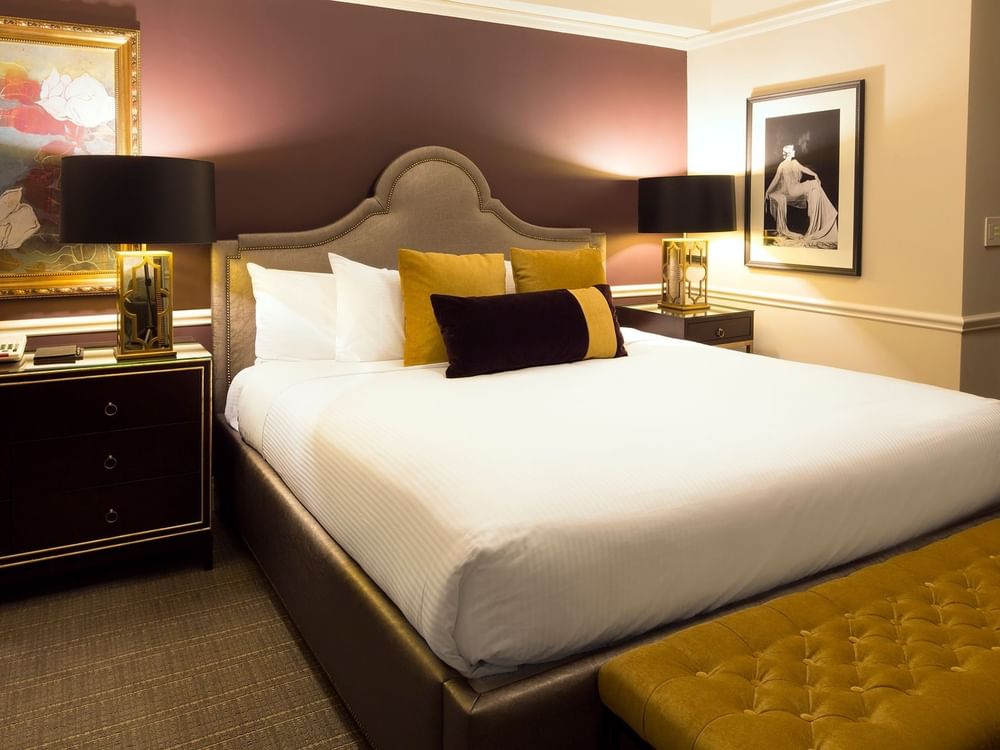 Bed between table lamps with gold pillows, and a deep purple accent wall behind in Follie Suite at Warwick New York