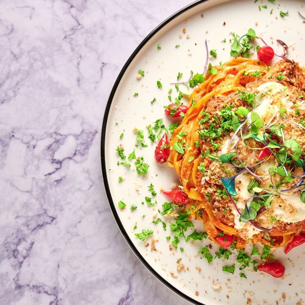 A pasta dish with tomatoes, cheese, and fresh herb garnishes on a rustic plate on a marble surface.