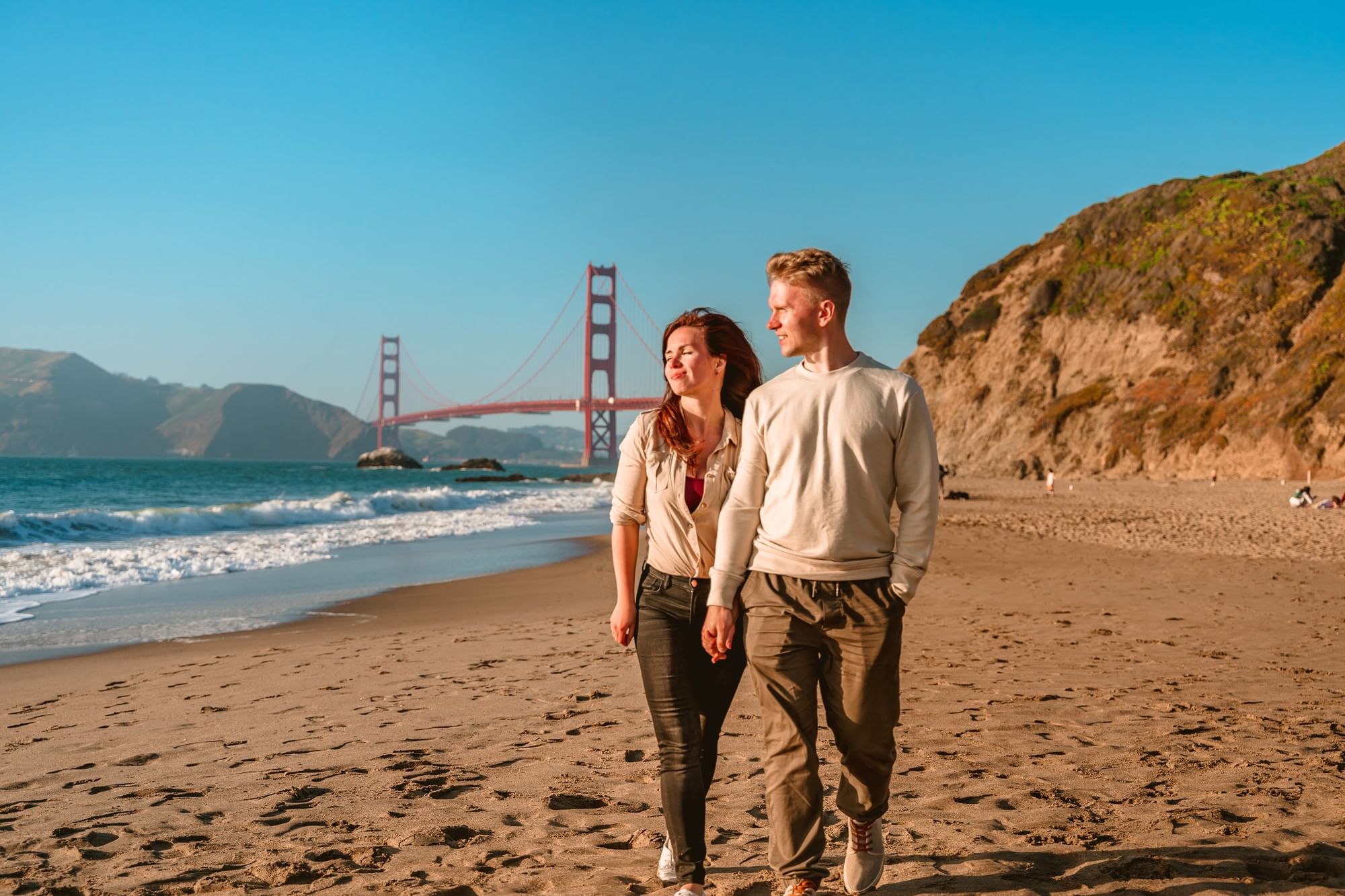 Couple walking on a sandy beach by the ocean under the Golden Gate Bridge near Warwick San Francisco
