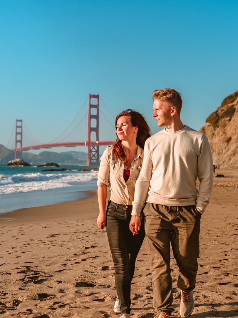 Couple walking on a sandy beach by the ocean under the Golden Gate Bridge near Warwick San Francisco