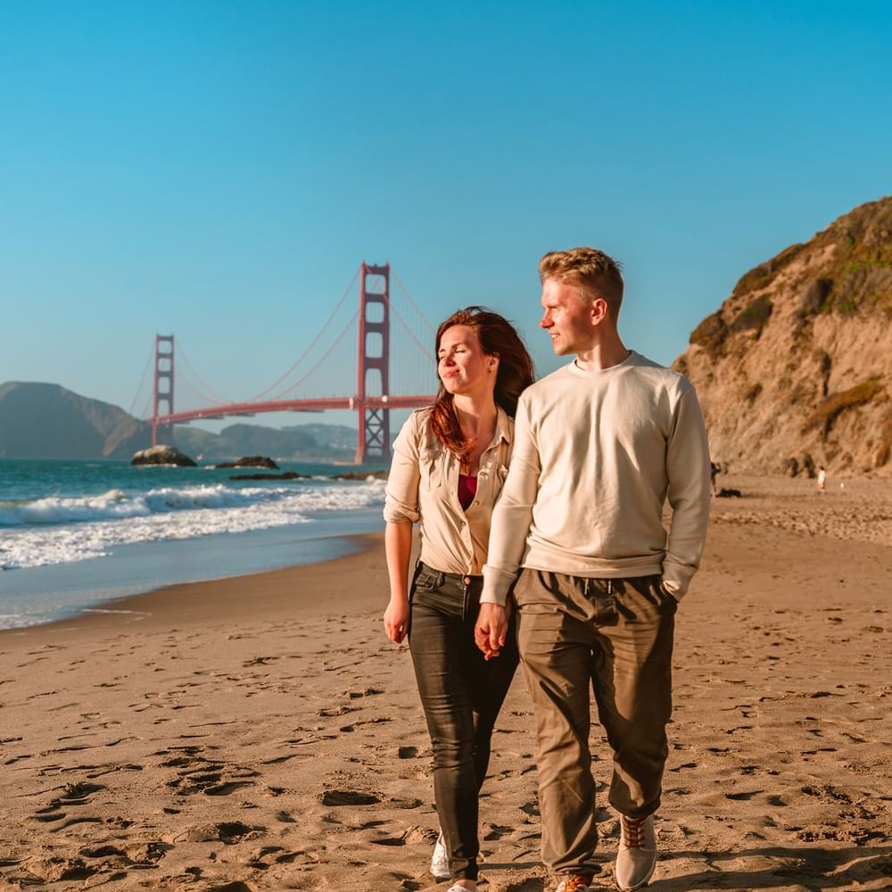 Couple walking on a sandy beach by the ocean under the Golden Gate Bridge near Warwick San Francisco