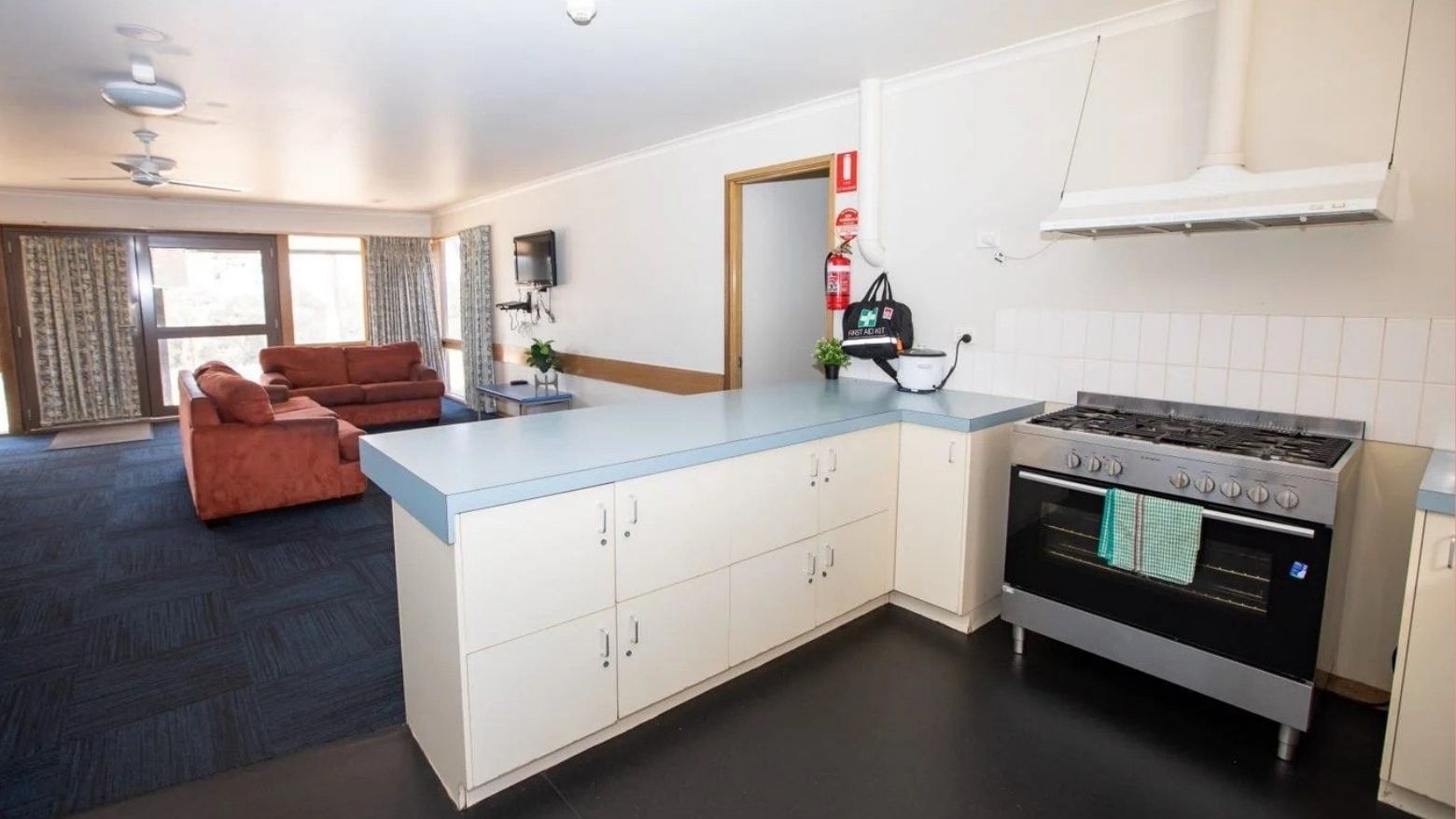 Open-plan living space with kitchen, oven, and red couches near a glass door.
