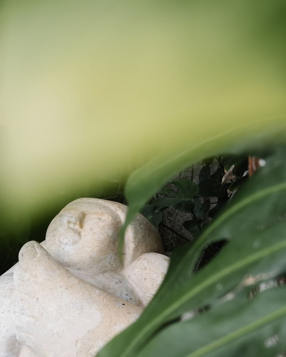 Stone sculpture of a sleeping figure nestled among lush tropical leaves at Morgan\'s Rock Reserve & Ecolodge