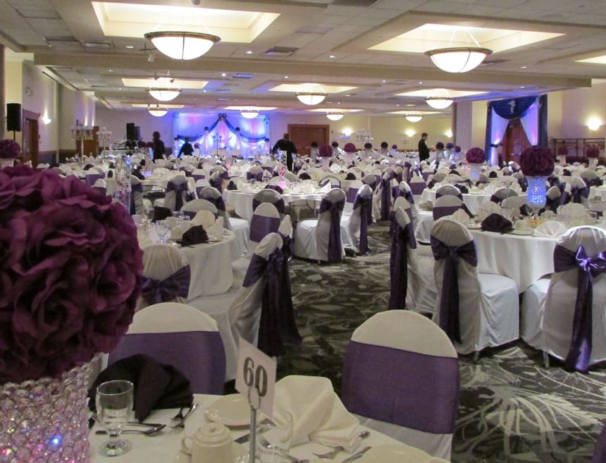 Round tables with purple sashed chairs by rose centerpieces, under pendant lighting at Glenmore Inn & Convention Centre