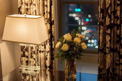 Close-up of a lamp & roses on a table in a room at Eliot Hotel