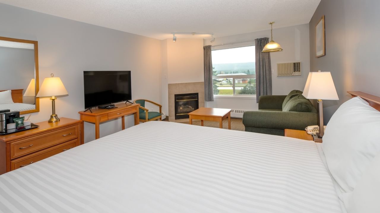 A hotel room with a large bed, green couch, flat-screen TV, and fireplace.