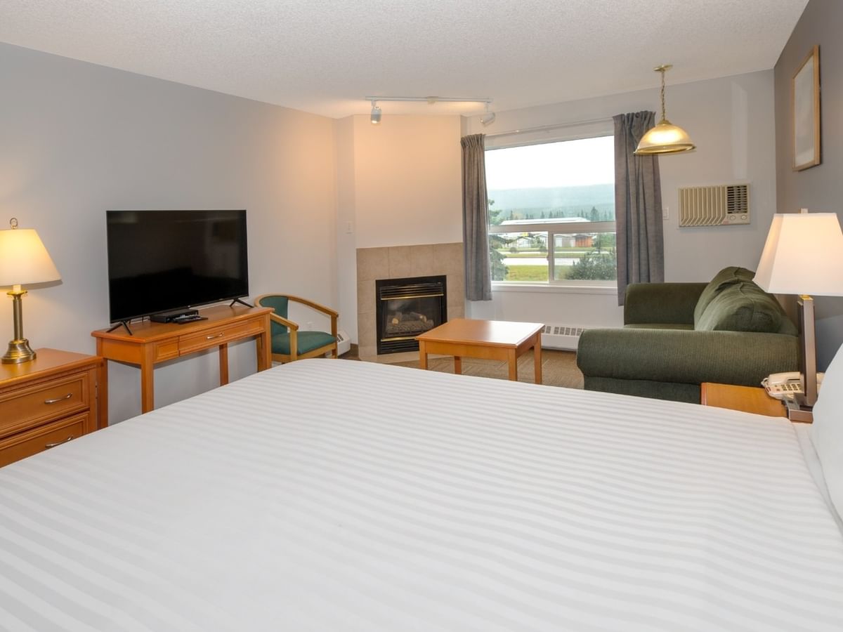 A bedroom with a large bed, couch, TV, fireplace, and window with a mountain view.