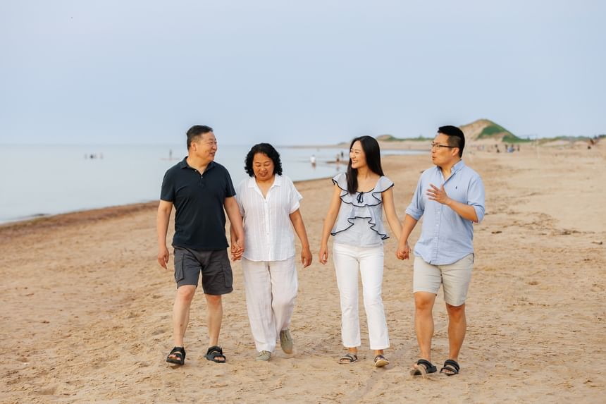 Four people walking hand-in-hand along a wide sandy beach shore at Rodd Crowbush Golf & Beach Resort