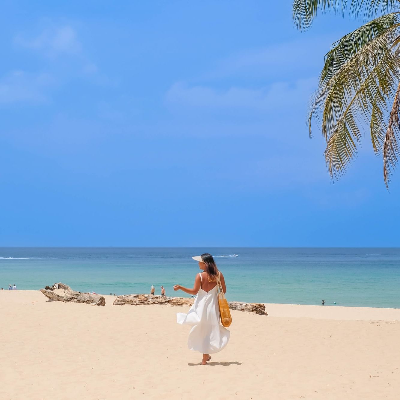 A woman is walking on the pristine white sand of Karon Beach with the view of crystal-clear blue sea