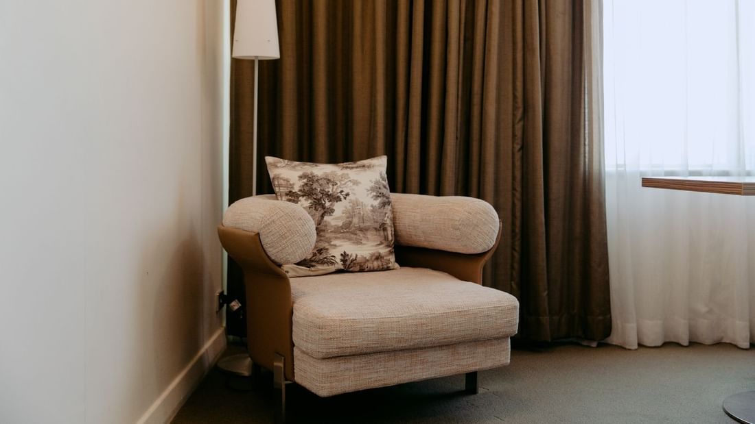 Armchair with a pillow in a room with a window, curtains, and a lamp.