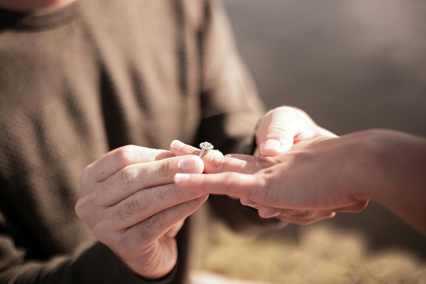 Close-up of a man's hands placing a diamond engagement ring on a woman's finger outdoors at Shangri-La Resort and Golf Club