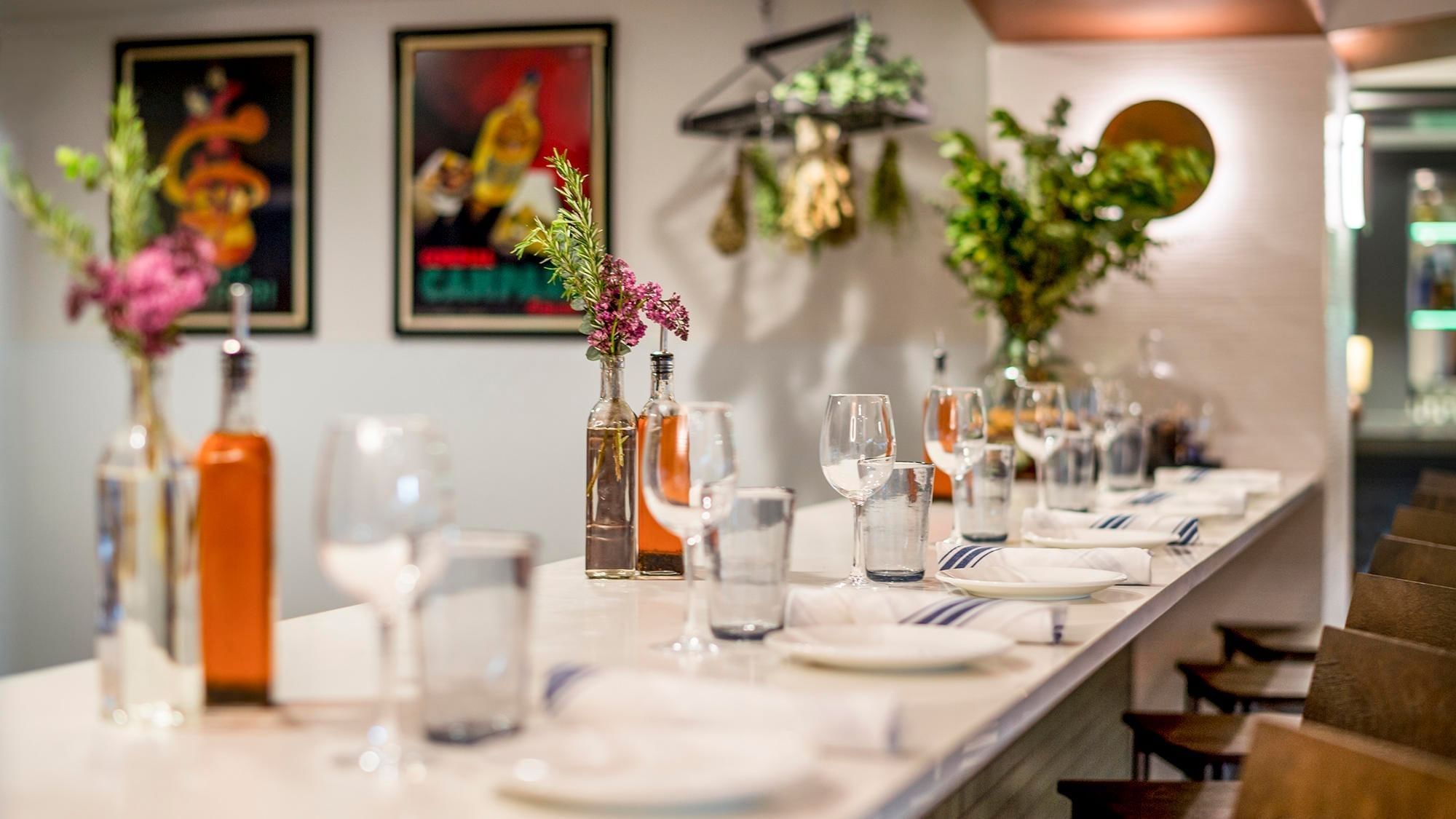 A long white table set with wine glasses, plates, and flowers in vases.