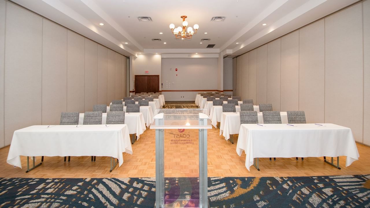 A large conference room with rows of tables and chairs, a podium, and a chandelier.