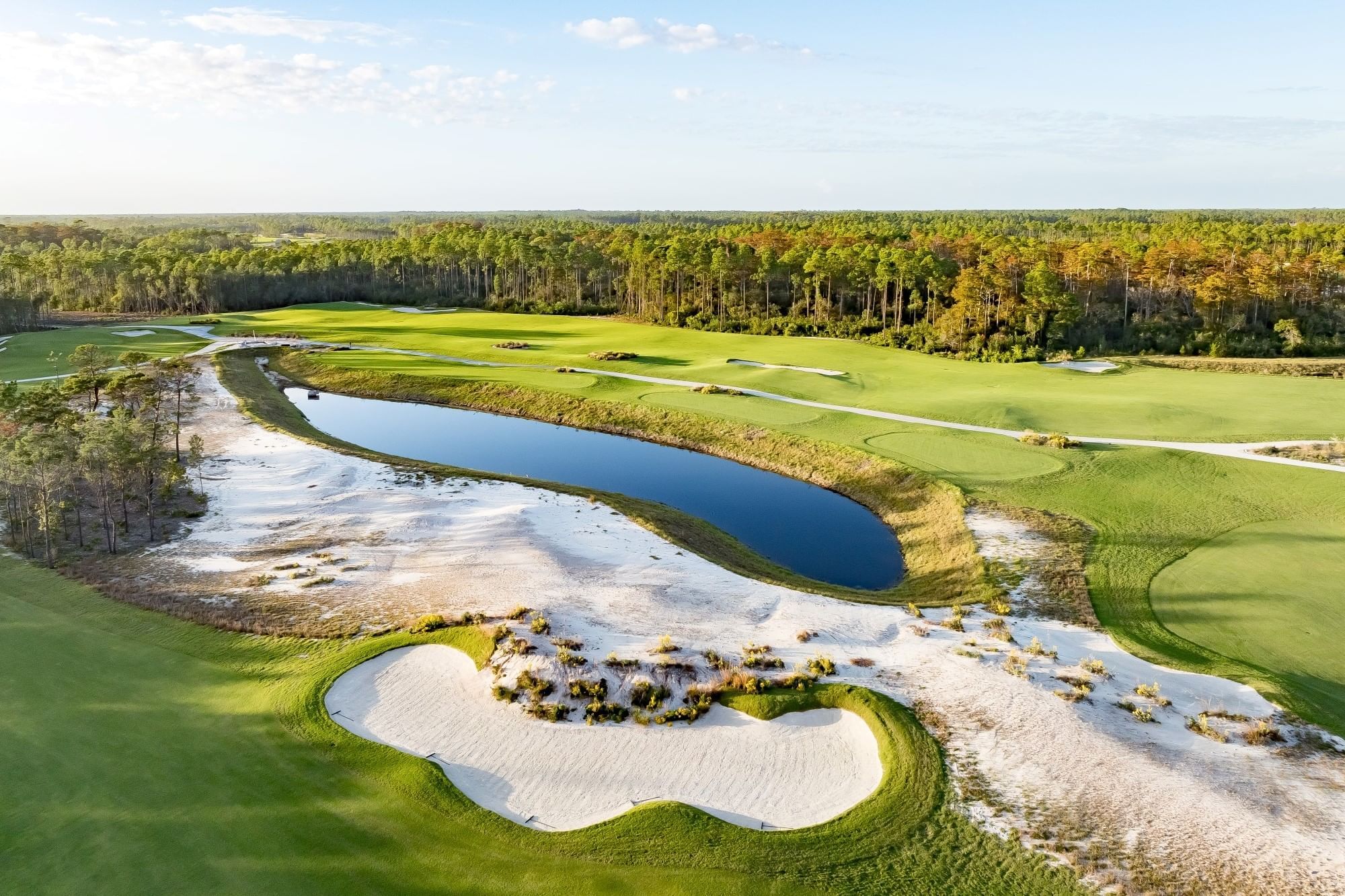 Aerial view of a golf course with a lake, sand traps, and green fairways surrounded by trees.