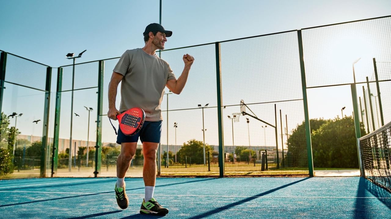 Mann auf einem Paddle-Tennis-Platz, mit Schläger in der Hand und siegreichem Ausdruck.