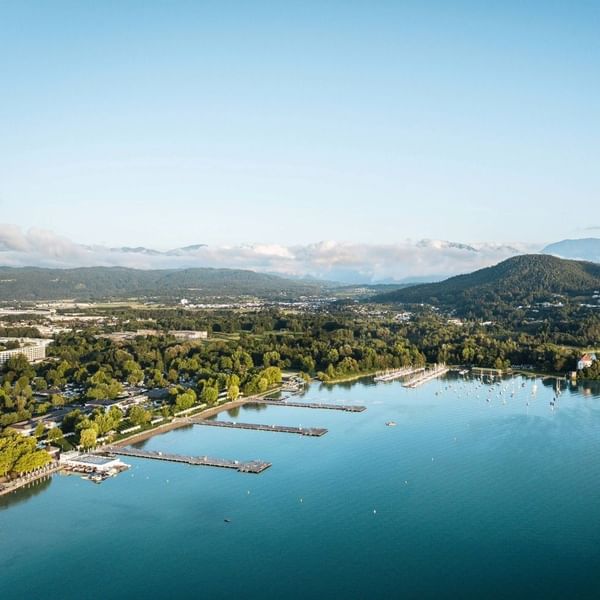 Aerial view of lake with marina, docked boats, and surrounding hills at Falkensteiner Camping Wörthersee