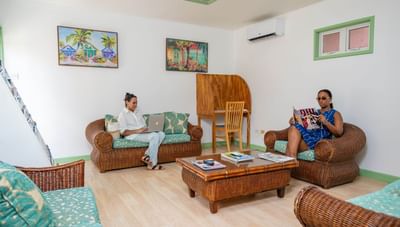 Two women relaxing on wicker furniture inside a bright and airy tropical lounge room at Worthing Court Apartment