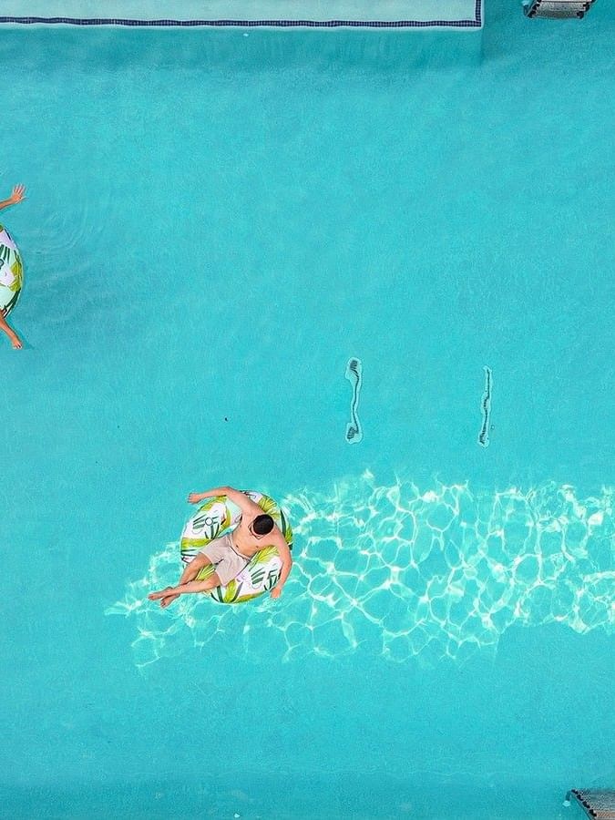 Two guests on leaf-patterned floats by the edge of a bright blue swimming pool side at Warwick Melrose Dallas