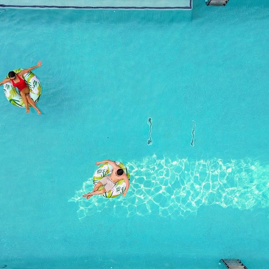Two guests on leaf-patterned floats by the edge of a bright blue swimming pool side at Warwick Melrose Dallas
