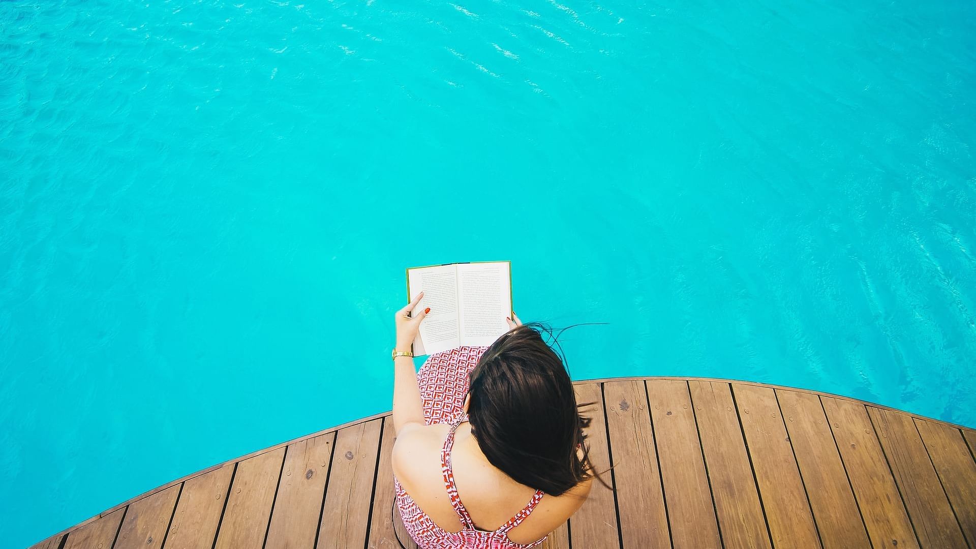 A lady reading a book on a pool deck at Originals Hotels
