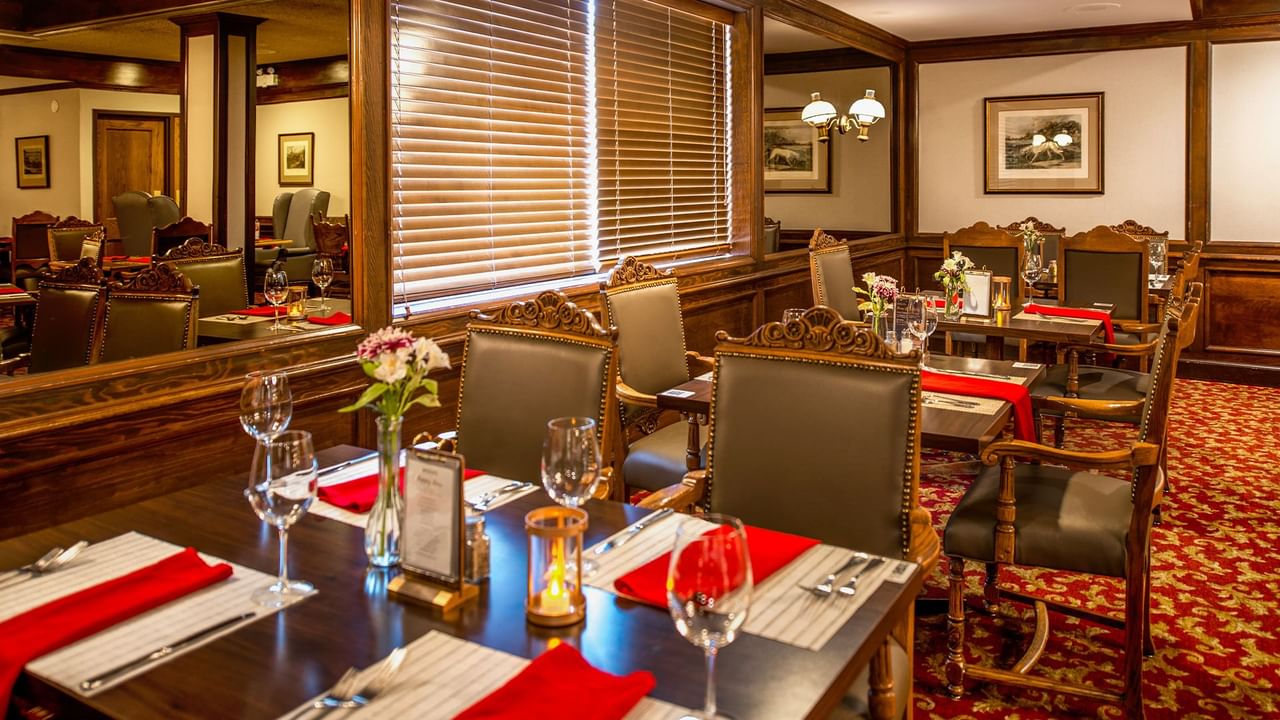 Elegant dining room with wooden tables, red napkins, and chairs.