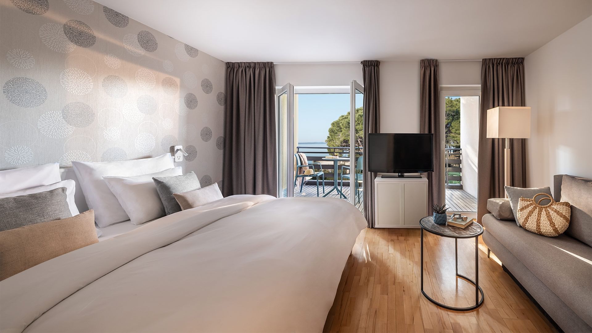 Elegant hotel room with a large bed, cozy couch, and balcony overlooking the sea at Falkensteiner Club Funimation Borik