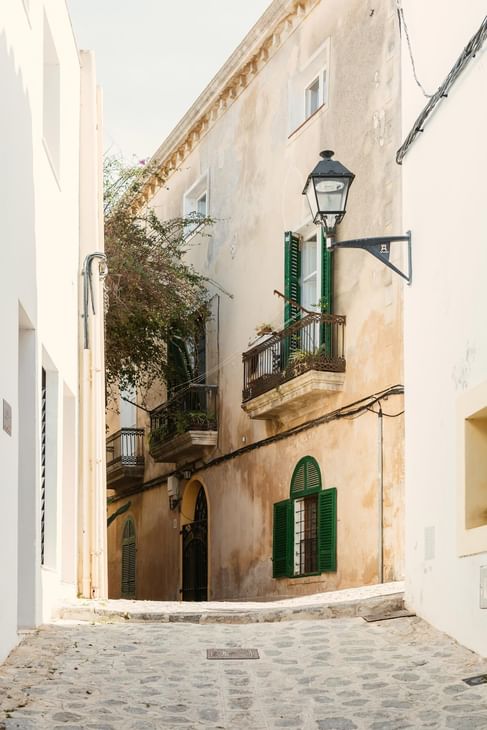 Ruelle pavée étroite avec bâtiments anciens et volets verts à Ibiza Gran Hotel