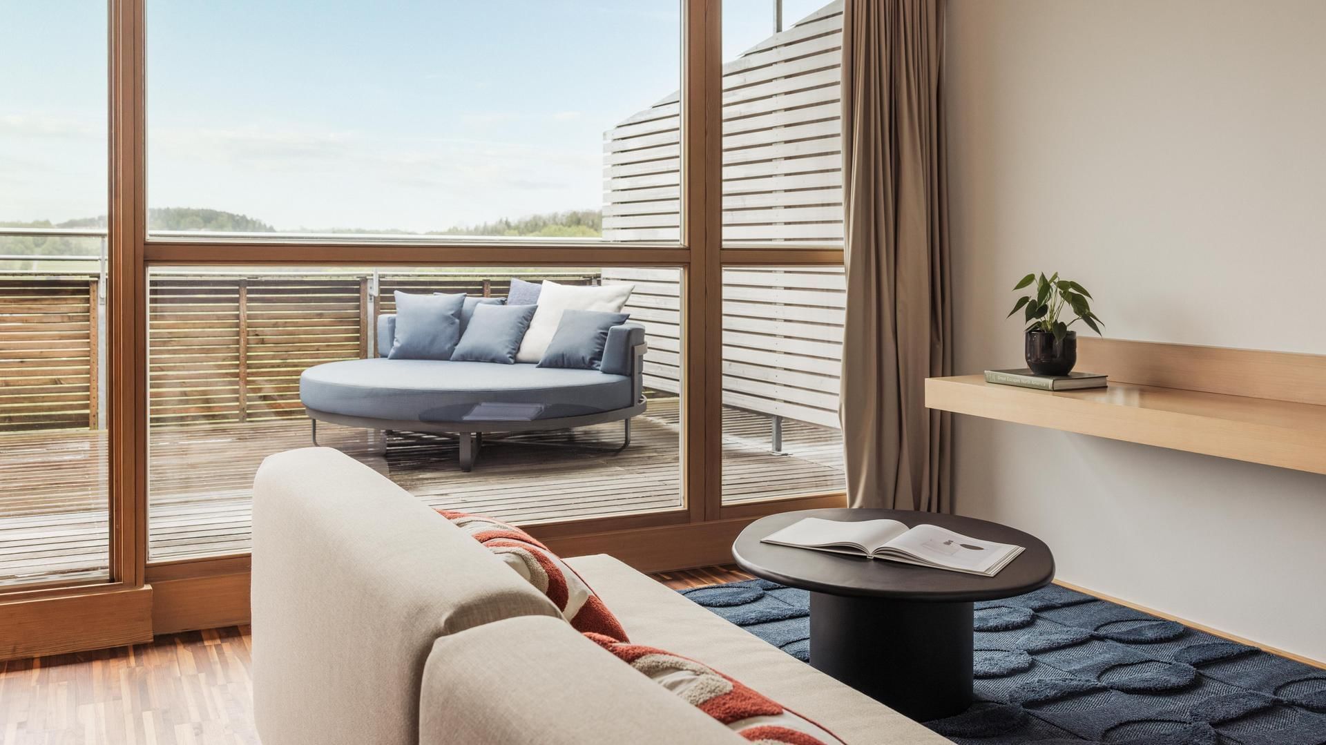 Modernes Zimmer mit Sofa, Couchtisch, Balkon und halbrundem Sitzbereich draußen.