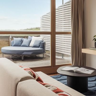 Modernes Zimmer mit Sofa, Couchtisch, Balkon und halbrundem Sitzbereich draußen.