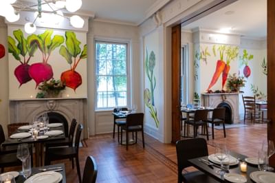 Elegant dining room with colorful vegetable murals, ornate fireplaces, and set tables at The Ashbrook Hotel