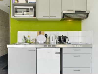 White kitchen with microwave, stove, and sink at Student Living Auckland - Beach.
