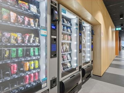 Three vending machines filled with drinks and snacks line a hallway at Mayoral Drive Student Accommodation.