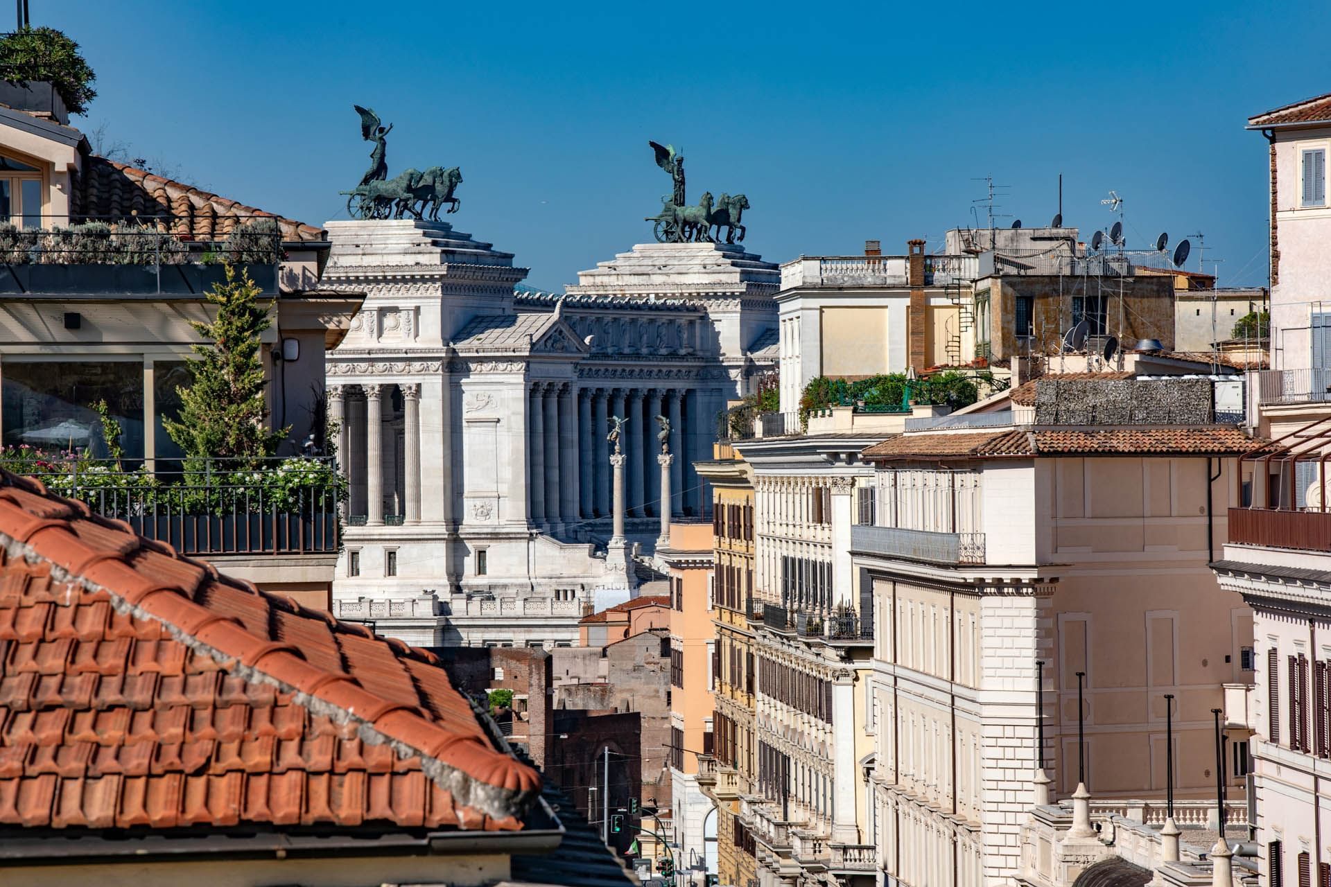 Victor Emmanuel II Monument framed by rooftops and buildings with statues atop the monument near The Glam Hotel