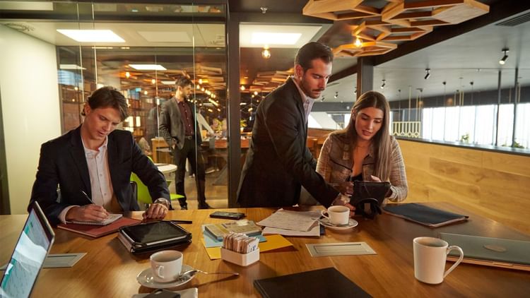 Three people working at a table with laptops and papers at Fiesta Americana