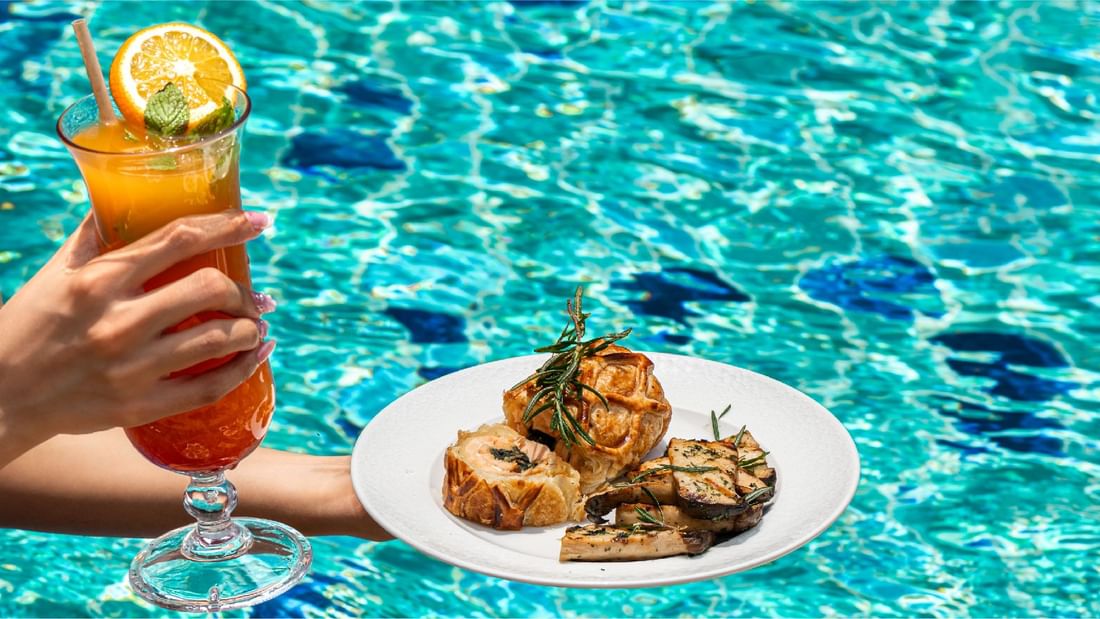 A lady holding a meat dish with a drink by a pool at Sunway Resort