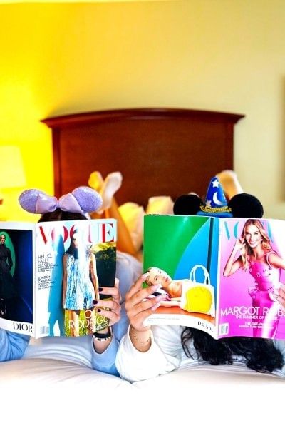 Two women read magazines while wearing Mickey ears lying on a bed at Rosen Inn Lake Buena Vista.