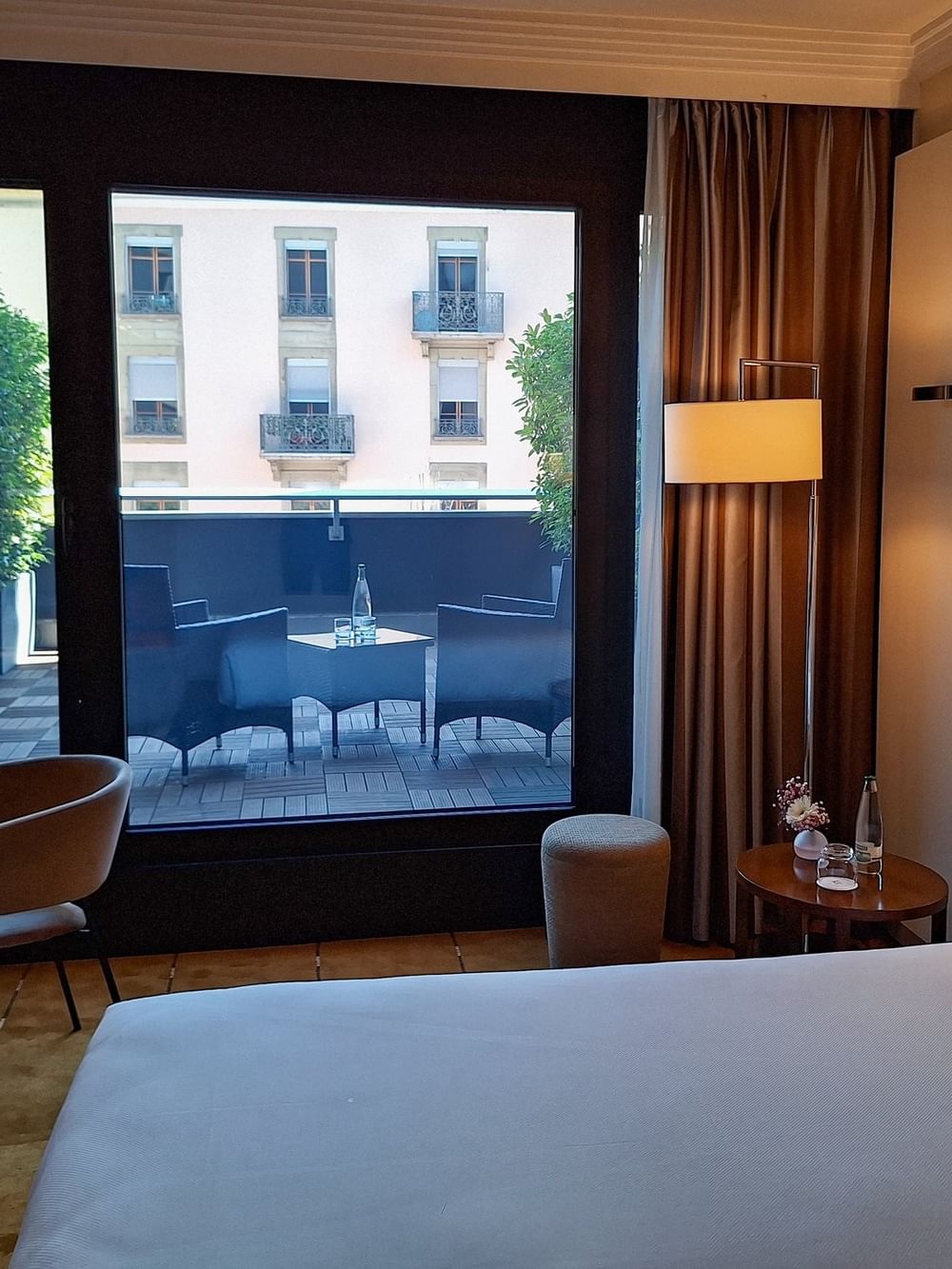Deluxe Terrace Room with a bed by a glass door opening to a private terrace & lounge chairs at Warwick Geneva