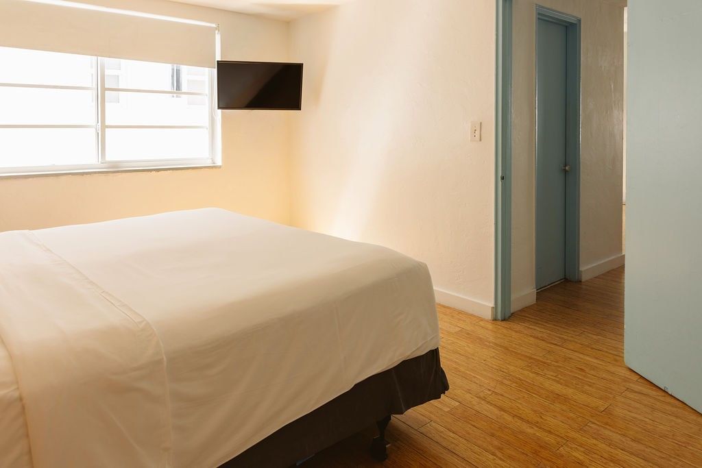 A hotel room with a bed, window, TV, and door.