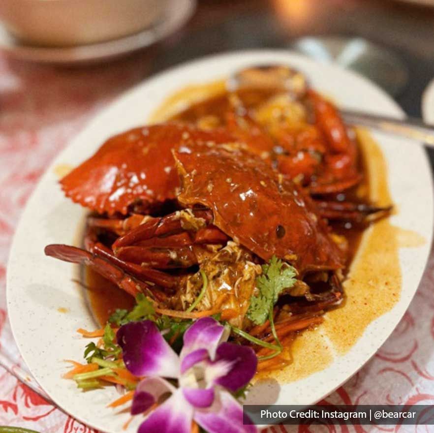 a plate of chili crab with a purple flower on the side