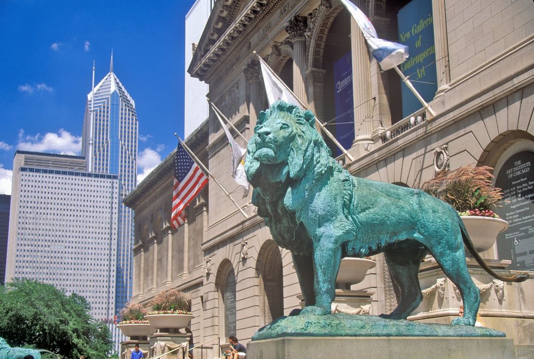 Bronze lion statue in front of a building with flags and skyscrapers near Warwick Allerton Chicago