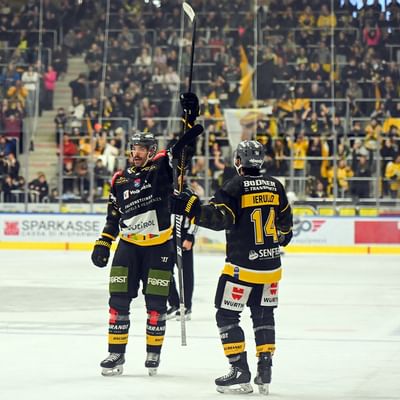 Giocatori di hockey su ghiaccio festeggiano con un bastone alzato, davanti a una folla di spettatori.