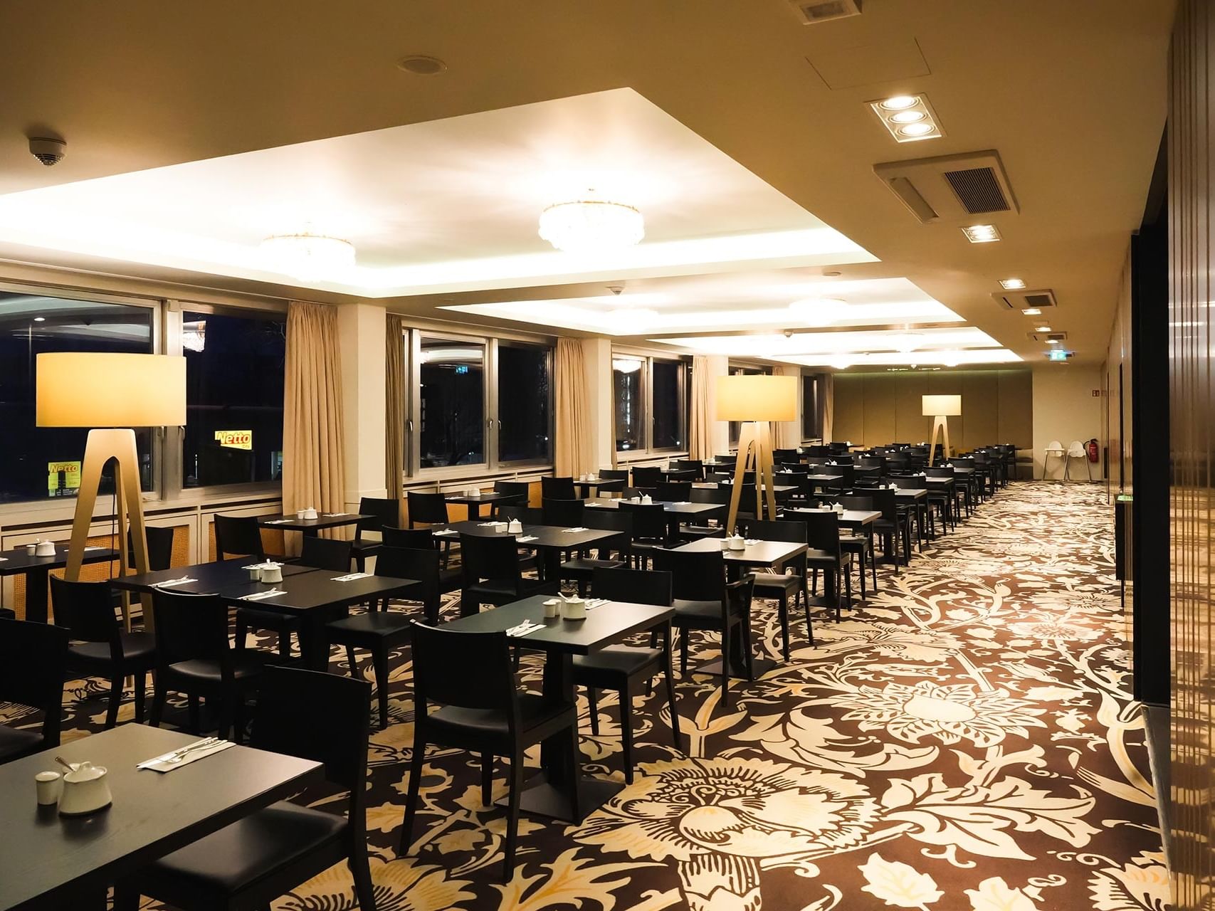 Breakfast area with tables and chairs, warm lighting, and patterned carpet at Sylter Hof Berlin.
