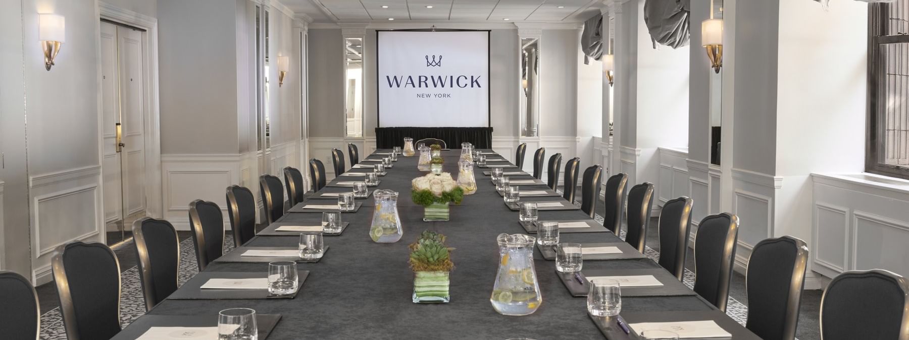 Close-up of a long conference table with purple flowers & glass sets in Essex meeting room at Warwick New York