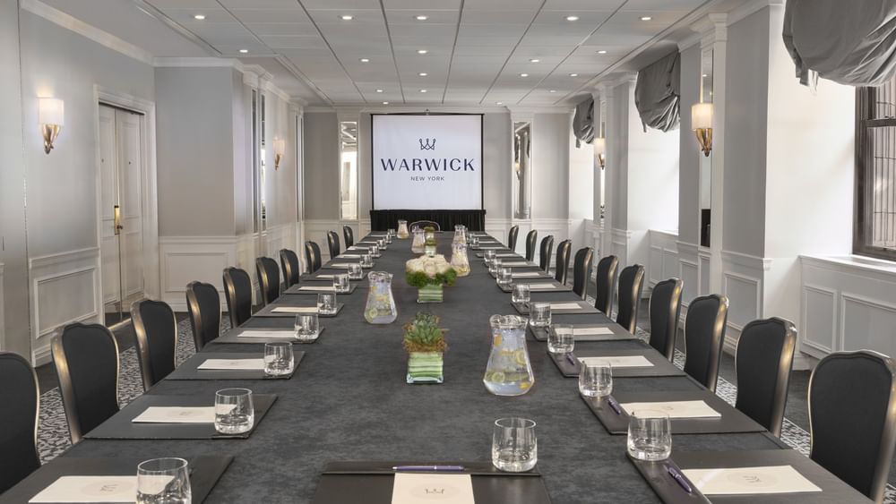 Close-up of a long conference table with purple flowers & glass sets in Essex meeting room at Warwick New York