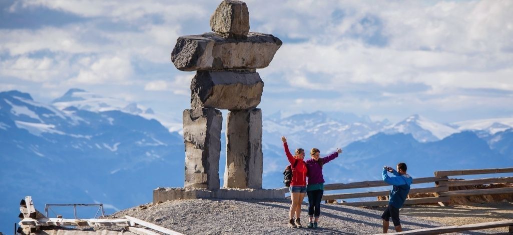Visitors posing beside an inukshuk with mountain views in Whistler