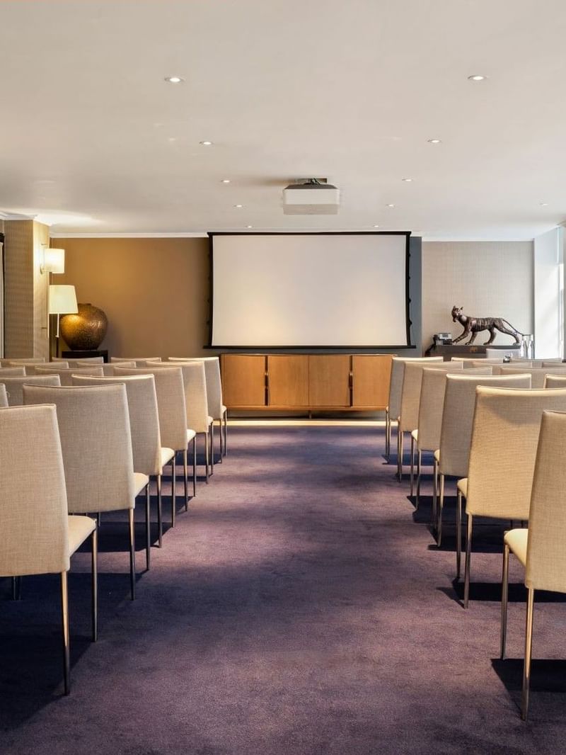 Event room with theater seating and a projector screen for presentations at The May Fair Hotel