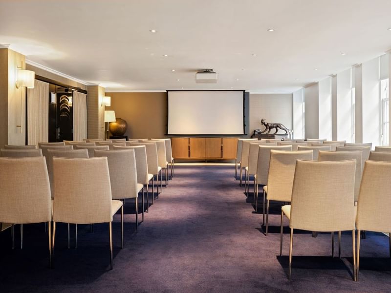 Event room with theater seating and a projector screen for presentations at The May Fair Hotel