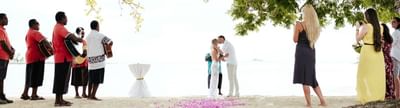 A beach wedding scene with a couple holding hands and musicians on the side at Musket Cove Island Resort & Marina